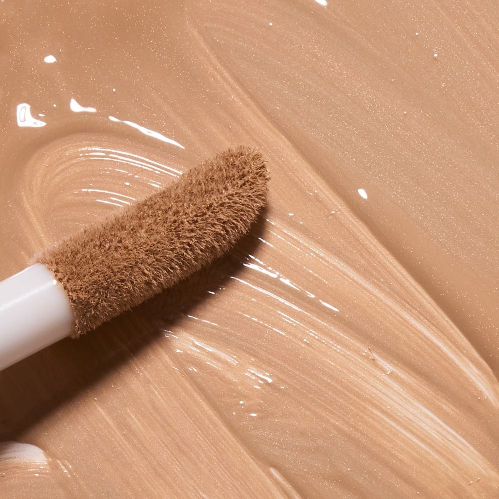 Brauner Concealer mit Schwammapplikator auf Haut